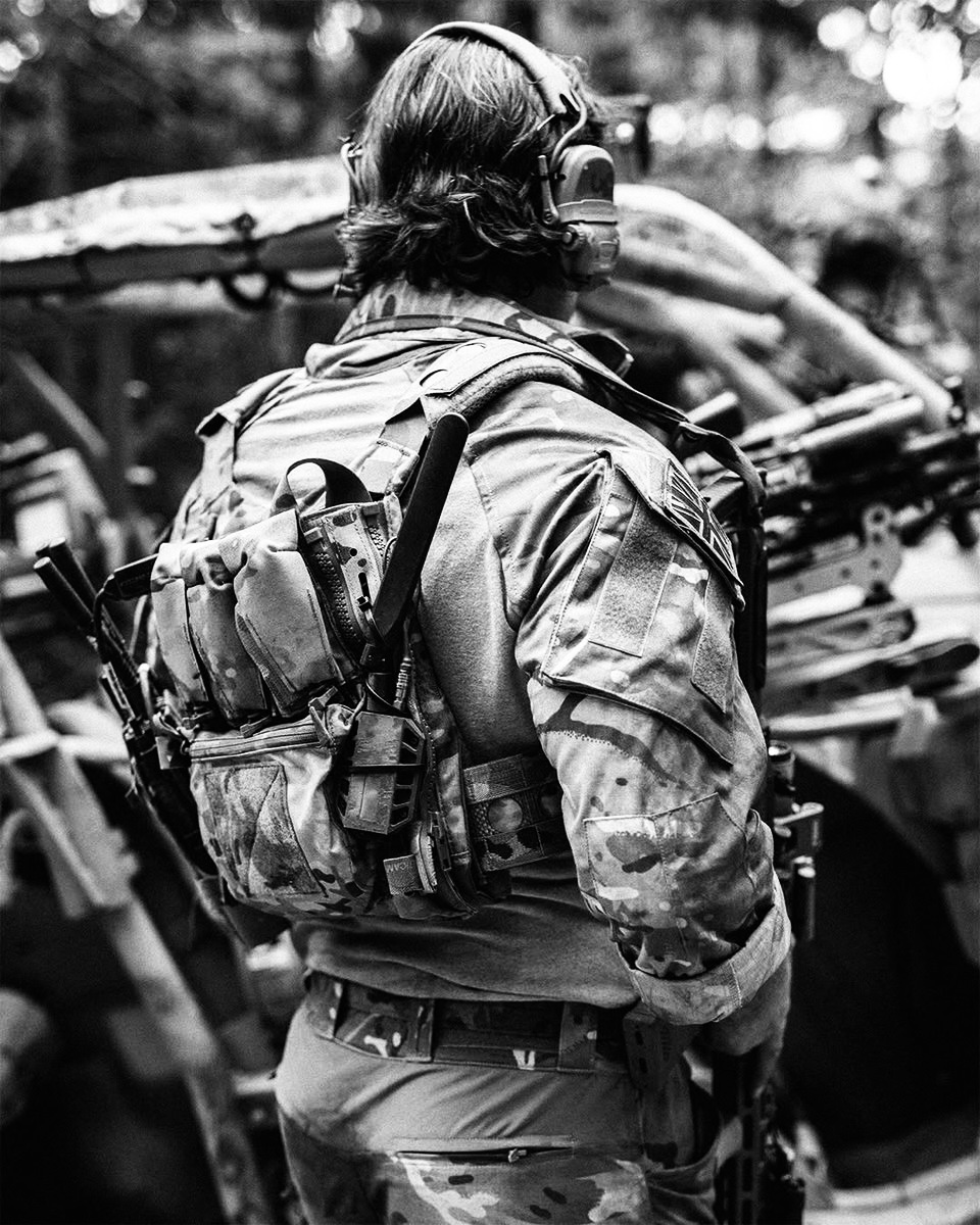 Operator in plate carrier and camouflage standing beside a vehicle